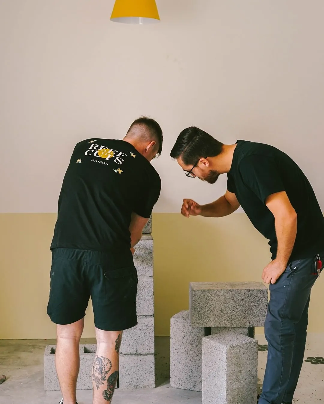 Two men standing with their back turned measuring cinder blocks 